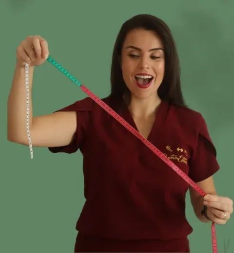 Josiéle, de jaleco bordô, medindo a cintura com uma fita métrica e sorrindo